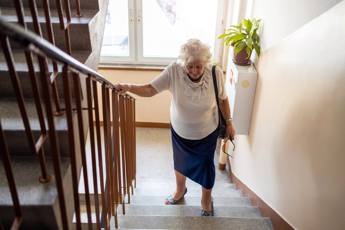Mujer mayor subiendo escaleras con dificultad, reflejando la limitación que el dolor de cadera puede imponer al movimiento cotidiano